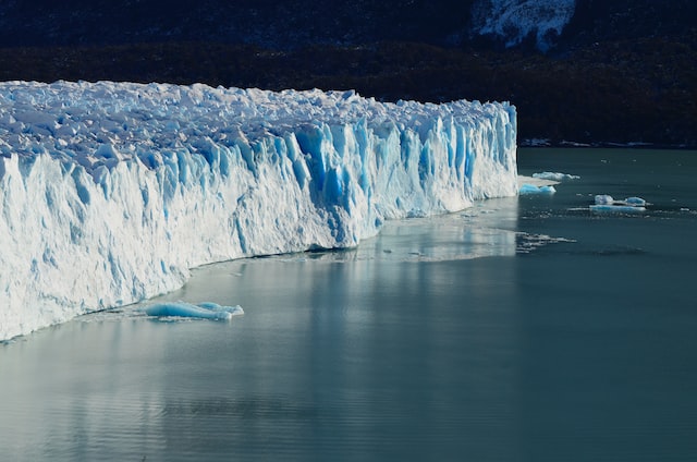 Large white glacier with blue tones surrounded by water.