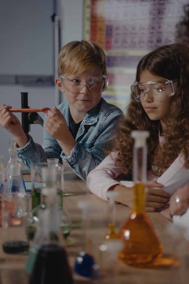 Two children with safety glasses sitting next to each other exploring chemistry.