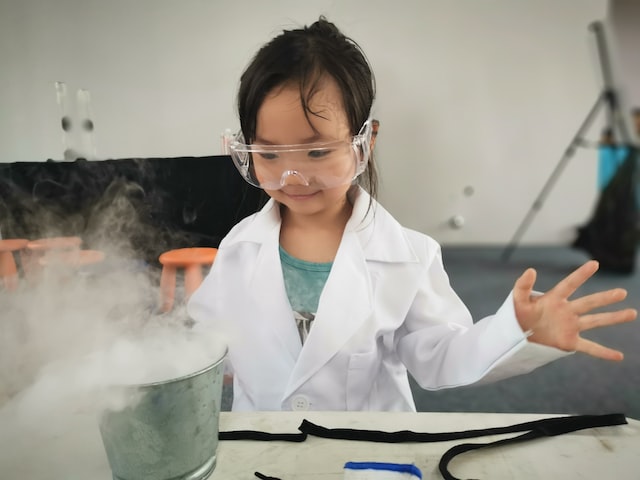 A girl in a white coat and glasses, experimenting with chemistry.